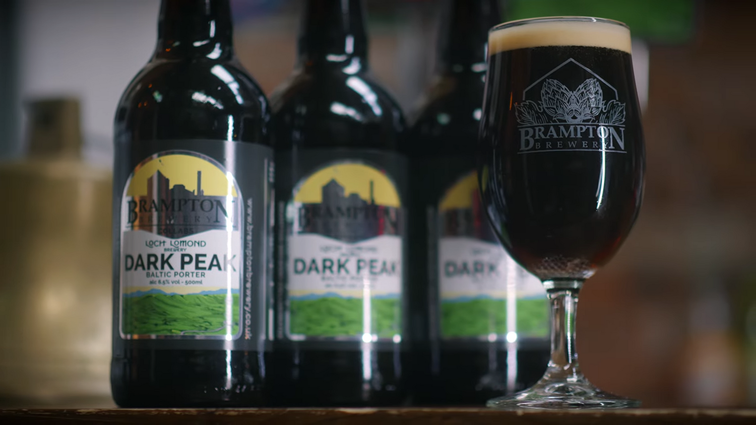 Dark Peak Baltic Porter beer by Brampton Brewery - three bottles lined up behind a glass filled with the dark beer, featuring a creamy head and the Brampton Brewery logo etched on the glass.