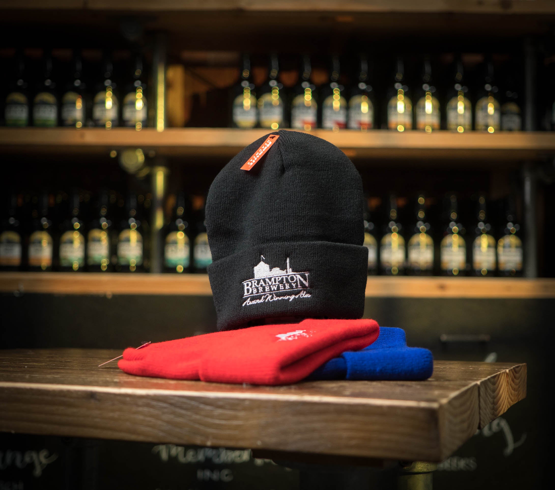 Black beanie with a Brampton Brewery logo on a wooden surface with bottles in the background