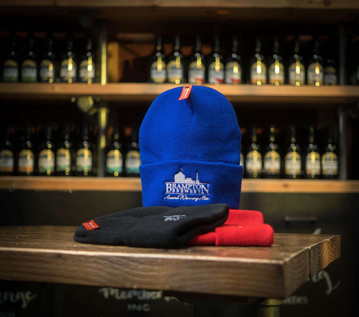 Blue beanie with a Brampton Brewery logo on a wooden surface with bottles in the background