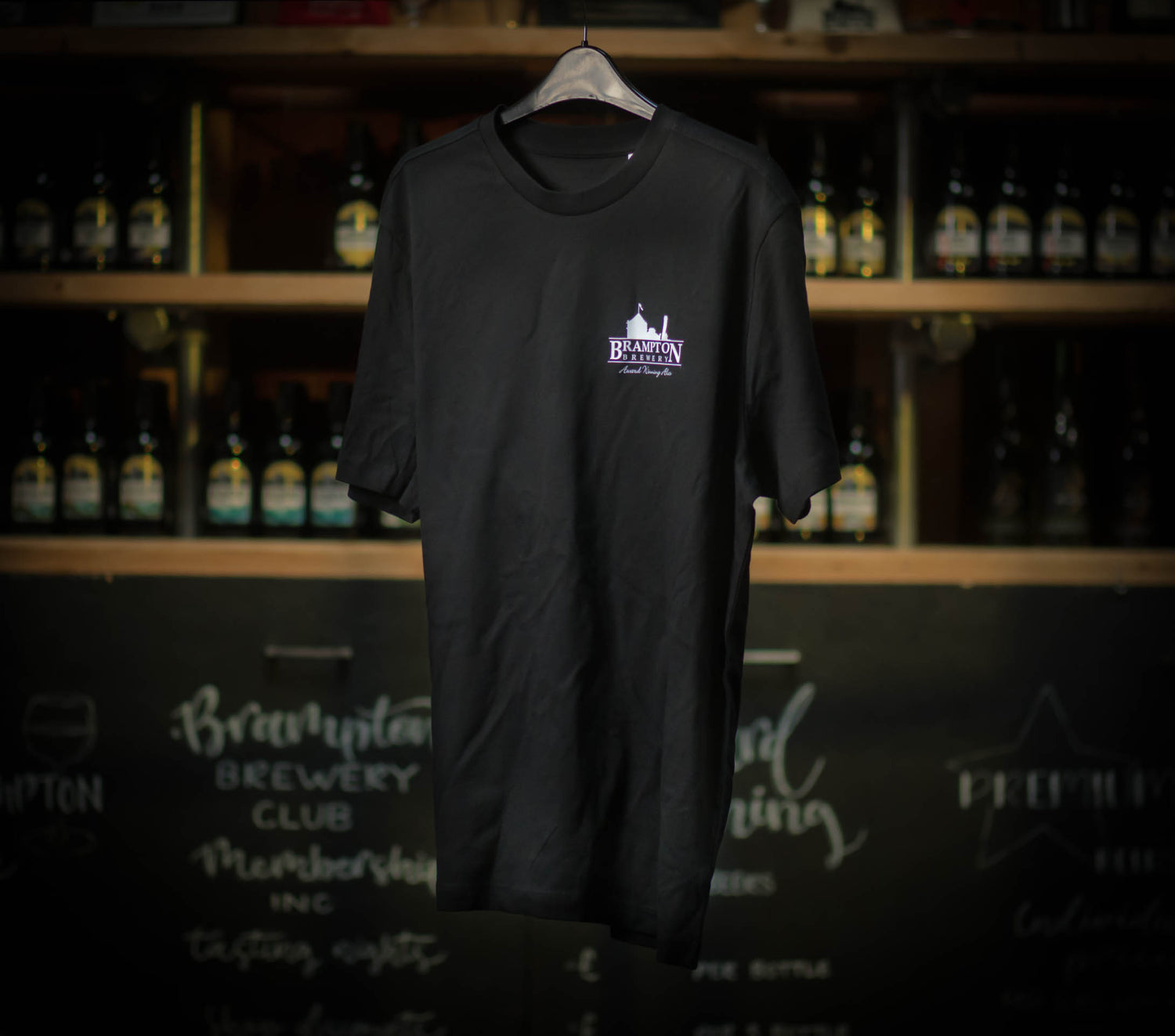 Black Brampton Brewery T‑shirt hanging in a rustic brewery setting, featuring the brewery’s logo and “Award Winning Ales” text.