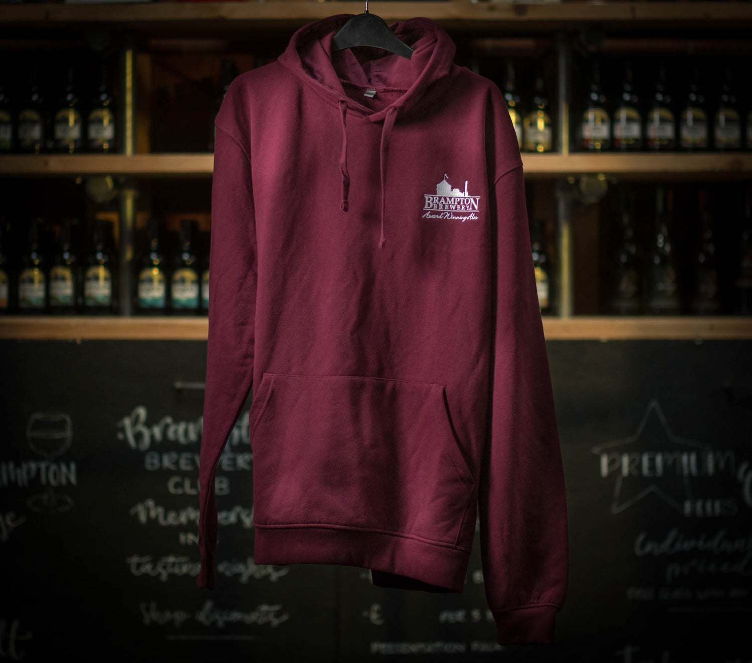 Maroon hoodie with a Brampton Brewery logo on a hanger against a backdrop of bottles