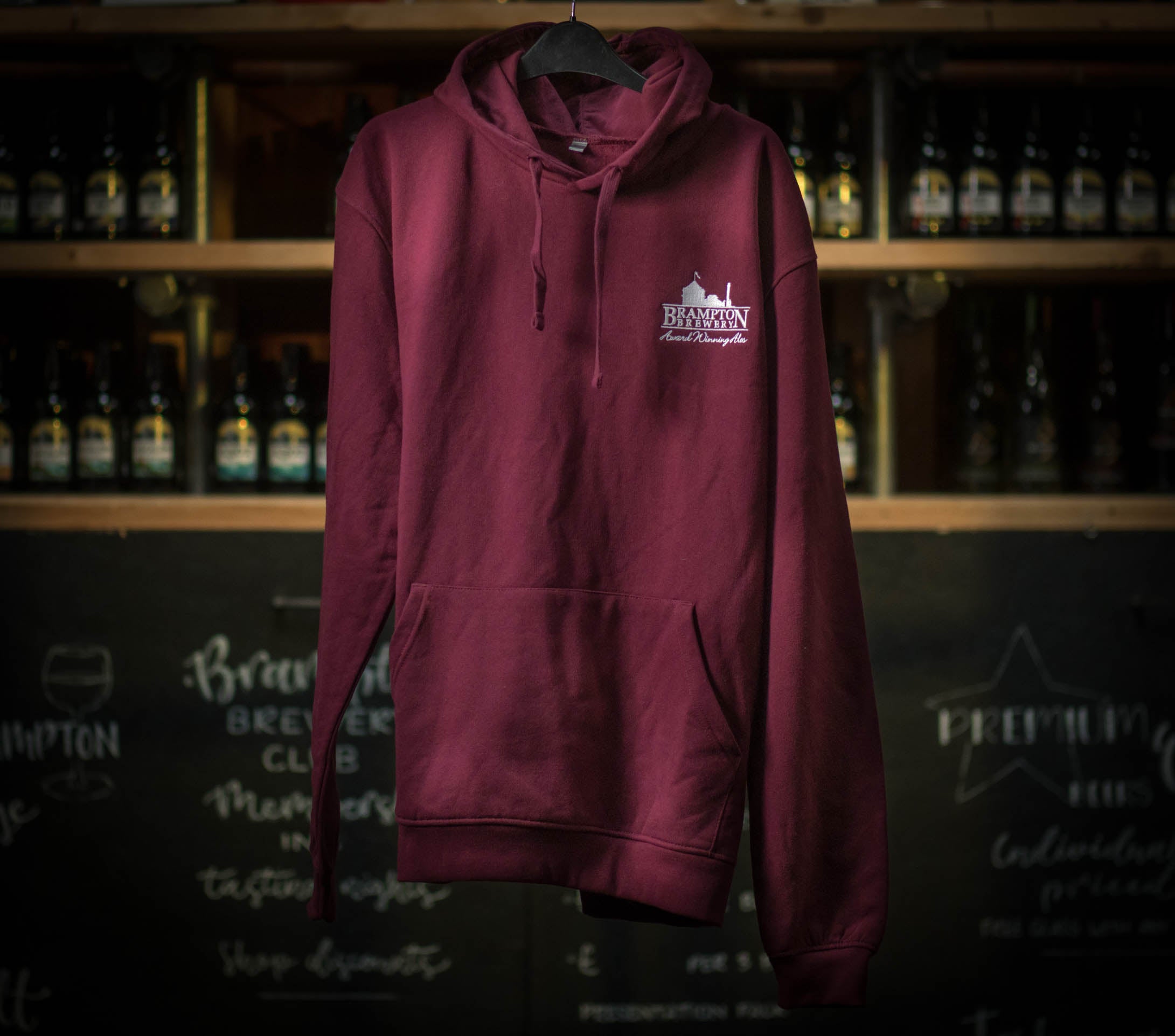 Maroon hoodie with a Brampton Brewery logo on a hanger against a backdrop of bottles