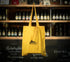 Yellow tote bag with a Brampton Brewery logo hanging in front of a shelf of bottles.